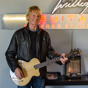 Paul Hanson Artist with Atlantis Guitar in front of logo